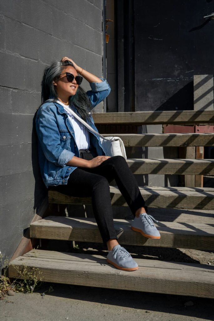 Woman in blue jacket and black pants sitting on brown wooden bench